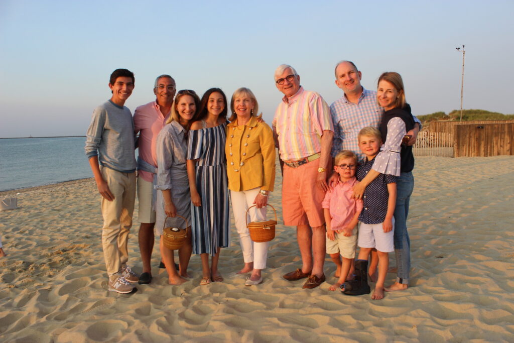 A group of nine people poses on the beach, smiling, with the ocean in the background during sunset.