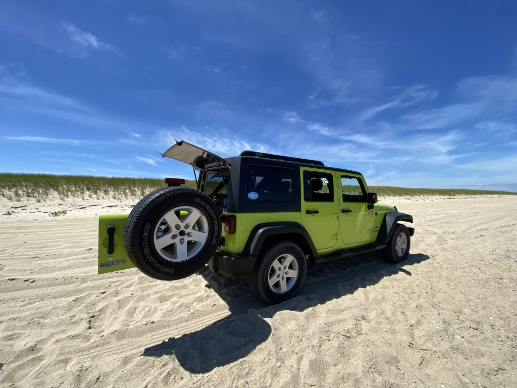 A bright green Jeep parked on sandy beach, with the rear door open and a spare tire visible.