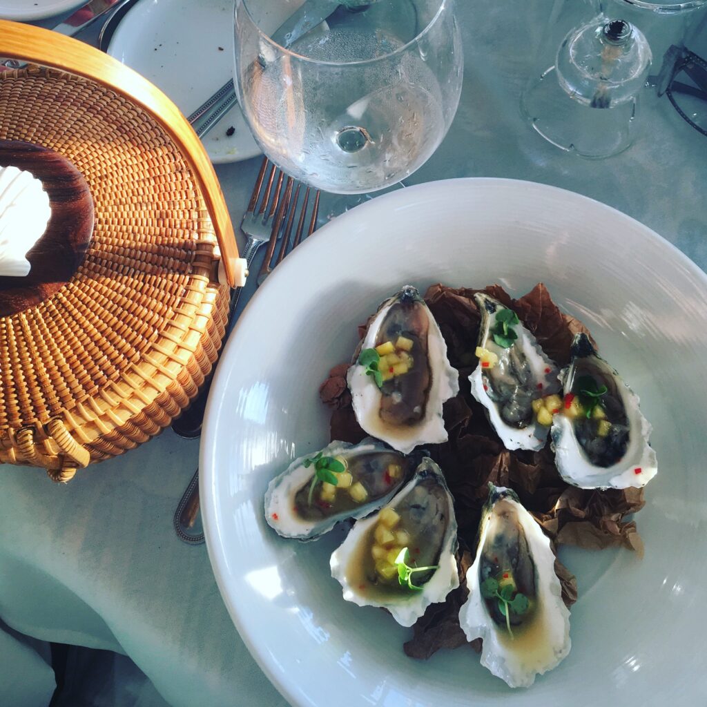 A plate of oysters garnished with diced fruit, next to a woven basket and a glass of water.
