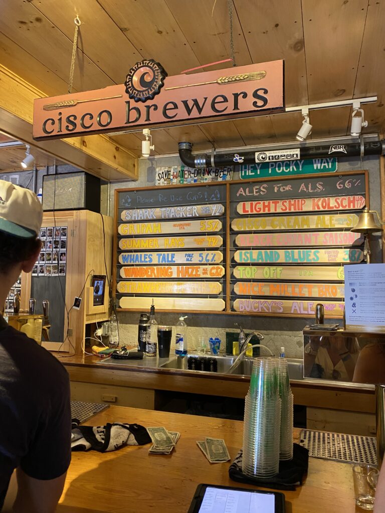 A bar counter displays a menu of craft beers with a customer standing nearby, cash on the counter.