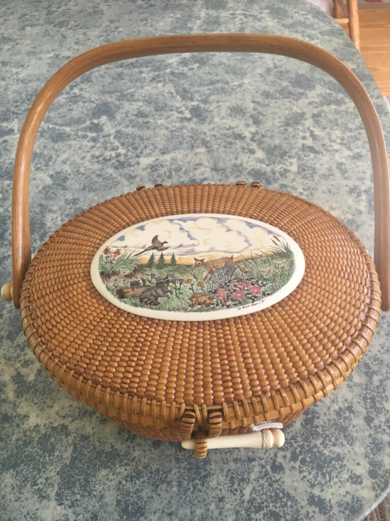 Woven basket with a decorative lid featuring a nature scene and a wooden handle.